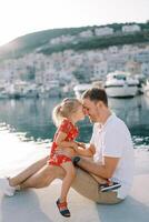 poco ragazza si siede su sua papà giro con sua naso toccante lui su il passerella di il mare foto