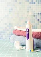 irrigatore elettronico per denti, spazzolini da denti e una pila di asciugamani vista frontale copia spazio