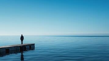 un' solitario figura sta a il bordo di un' bacino guardando su a il infinito distesa di blu acqua foto