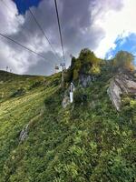 sbalorditivo Visualizza di un' cavo auto ascendente un' lussureggiante verde montagna sotto un' drammatico nuvoloso cielo, in mostra della natura bellezza foto