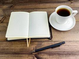 caffè nel un' tazza e un' taccuino con un' penna su un' di legno tavolo. foto