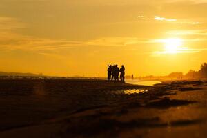 silhouette di un' gruppo di amici godendo il tramonto su il spiaggia a d'oro tramonto volta, rilassante su un' rilassante vacanza, mare nel il sera. foto