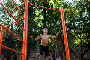 un atleticamente costruito bambino nel il parco cerca per saltare su e afferrare il traversa. strada allenarsi su un' orizzontale bar nel il scuola parco. foto