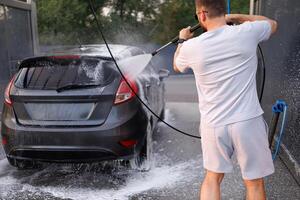 un' uomo sta indietro e lavaggi il indietro di il auto con un' acqua cannone. un' auto a un' se stesso servizio auto lavare. foto