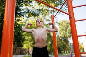 un' adolescente ragazzo di un atletico costruire Spettacoli il suo muscoli. strada allenarsi su un' orizzontale bar nel il scuola parco. foto