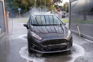 il davanti di un' lavato macchina, con un' uomo lavaggio il auto nel il sfondo. un' auto a un' se stesso servizio auto lavare. foto
