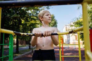 bambino detiene su corrimano gli sport attrezzatura strada allenarsi su un' orizzontale bar nel il scuola parco. foto