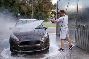 un' uomo punti un' acqua cannone a il cappuccio di un' macchina. un' auto a un' se stesso servizio auto lavare. foto