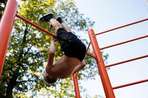 parte inferiore Visualizza di un' adolescente chi esegue ginnastica esercizi. strada allenarsi su un' orizzontale bar nel il scuola parco. foto