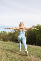 il ragazza atleta esegue il passaggi di affondo inoltrare. bellissimo bionda caucasico donna nel blu stretto tuta. bionda ragazza a un all'aperto formazione sessione foto