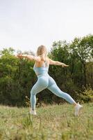 lato Visualizza di un atletico ragazza l'esecuzione inoltrare affondi nel il parco. bellissimo bionda caucasico donna nel blu stretto tuta. bionda ragazza a un all'aperto formazione sessione foto