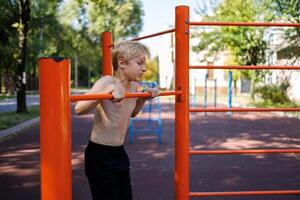 un' in forma bambino eseguita un' sport pull-up su il sbarra. strada allenarsi su un' orizzontale bar nel il scuola parco. foto