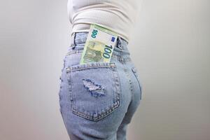 c'è un' centinaio Euro conto attaccare su di il indietro tasca di il suo jeans. un' ragazza nel jeans con un' Euro banconota nel sua mani. foto