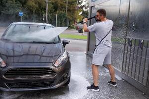 un' uomo punti un' acqua cannone a il parabrezza di un' macchina. un' auto a un' se stesso servizio auto lavare. foto