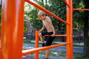 un' fitness bambino scalato fra il gli sport barre. strada allenarsi su un' orizzontale bar nel il scuola parco. foto