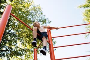 un' adolescente chi ha scalato un' ginnastica bar si siede e riposa. strada allenarsi su un' orizzontale bar nel il scuola parco. foto