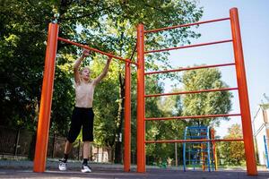 un atletico adolescente prepara per eseguire un esercizio. strada allenarsi su un' orizzontale bar nel il scuola parco. foto
