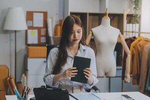 ritratto bellissimo Sorridi asiatico progettista donna uso computer nel sarto tessuto moda piccolo attività commerciale in linea officina. giovane proprietario avviare imprenditore. creativo ragazza tessile indumento pmi attività commerciale concetto foto