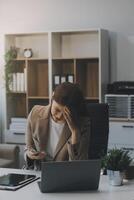 asiatico donne seduta nel un ufficio con fatica e occhio sforzo stanco, ritratto di triste infelice stanco frustrato deluso signora sofferenza a partire dal emicrania seduta a il tavolo, malato lavoratore concetto foto