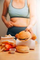 per mangiare o non. triste paffuto donna guardare a il hamburger mentre pensiero per mangiare esso o non foto