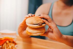 abbuffata mangiare disturbo concetto con donna mangiare veloce cibo hamburger, licenziato pollo , ciambelle e dolci foto