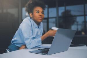 annoiato giovane donna nel il ufficio Lavorando con un' il computer portatile e fissando a computer schermo foto