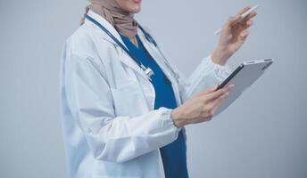 medico indossare bianca cappotto e Guardando paziente dati nel tavoletta . foto