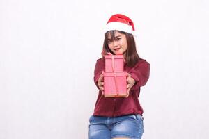 bellissimo giovane asiatico indonesiano ragazza sorridente portando regalo scatola a Natale Santa Claus cappello moderno rosso camicia attrezzatura dando i regali i regali su bianca sfondo per promozione e pubblicità foto
