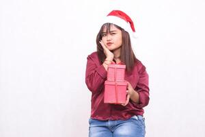 bellissimo giovane grazioso sud-est asiatico ragazza trasporto regalo scatola a Natale indossare Santa Claus cappello moderno rosso camicia attrezzatura Tenere guance bianca sfondo per promozione e pubblicità foto