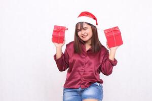 bellissimo giovane asiatico indonesiano ragazza trasporto regalo scatola a Natale Santa Claus cappello moderno brillante rosso camicia attrezzatura guardare a telecamera su bianca sfondo per promozione e pubblicità foto