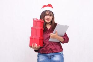 bellissimo giovane sud-est asiatico donna sorridente trasporto 3 regalo scatole ostacolare e tavoletta il computer portatile a Natale indossare Santa Claus cappello moderno rosso camicia attrezzatura bianca sfondo per promozione e pubblicità foto