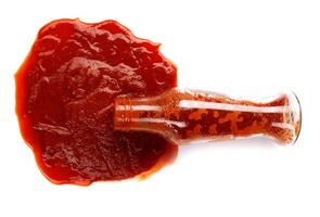 pomodoro salsa . bicchiere bottiglia con ketchup e un' pozzanghera di ketchup rovesciato in giro esso isolato su un' bianca sfondo. foto