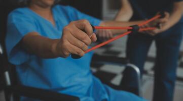 personale allenatore assistere anziano donna con resistenza gruppo musicale. reinserimento fisioterapia lavoratore porzione vecchio paziente a assistenza infermieristica casa. vecchio donna con allungare gruppo musicale essere allenato di fisioterapista. foto