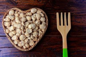 carne di soia, pezzi in un cesto a forma di cuore. pezzi di semi di soia crudi su fondo di legno rustico foto