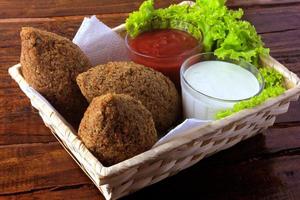 Kibbeh fritto con salsa di pomodoro in un cestello, su tavola in legno rustico foto