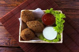 Kibbeh fritto con salsa di pomodoro in un cestello, su tavola in legno rustico foto