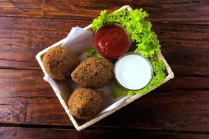 Kibbeh fritto con salsa di pomodoro in un cestello, su tavola in legno rustico foto