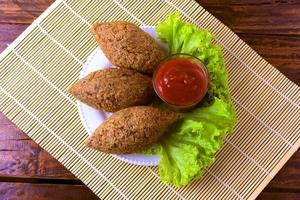 Kibbeh fritto con salsa di pomodoro su un piatto, su tavola in legno rustico foto