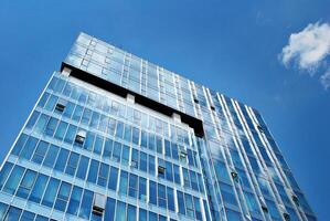 bicchiere edificio con trasparente facciata di il edificio e blu cielo. strutturale bicchiere parete riflettendo blu cielo. astratto moderno architettura frammento. contemporaneo architettonico sfondo. foto