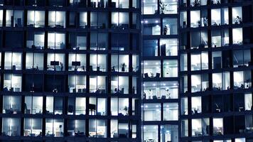 frammento di il bicchiere facciata di un' moderno aziendale edificio a notte. moderno bicchiere ufficio nel città. grande raggiante finestre nel moderno ufficio edifici a notte, nel righe di finestre leggero brilla. foto