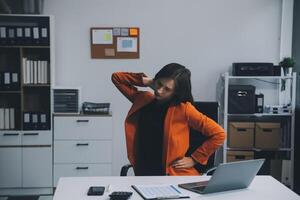 asiatico donna Lavorando difficile nel il ufficio avendo dolori e dolori nel sua torso e vita foto