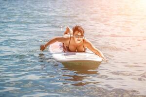 donna cenare mare viaggio. gli sport ragazza su un' tavola da surf nel il mare su un' soleggiato estate giorno. nel un' nero bagnarsi completo da uomo, lui si siede su un' sapa nel il mare. riposo su il mare. foto