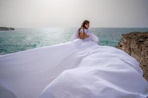 contento la libertà donna su il spiaggia godendo e in posa nel bianca vestire. posteriore Visualizza di un' ragazza nel un' svolazzanti bianca vestito nel il vento. vacanze, vacanze a mare. foto