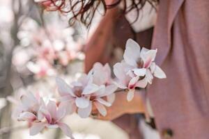 magnolia parco donna. elegante donna sta vicino il magnolia cespuglio nel il parco. vestito nel bianca corsetto pantaloni e in posa per il telecamera. foto