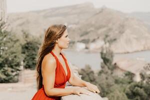 donna rosso vestire. estate stile di vita di un' contento donna in posa vicino un' recinto con balaustre al di sopra di il mare. foto