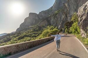 un' donna corre lungo un asfalto strada nel il mezzo di un' mountainou foto