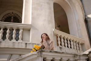 un' donna indossare occhiali da sole e Tenere un' mazzo di giallo fiori sta su un' balcone. il scena è tranquillo, calmo e sereno, con il donna guardare su al di sopra di il città. foto