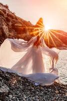 misterioso donna silhouette lungo capelli passeggiate su il spiaggia oceano acqua, mare ninfa vento ascolta per il onda. lanci su un' lungo bianca vestire, un' divine tramonto. artistico foto a partire dal il indietro senza un' viso