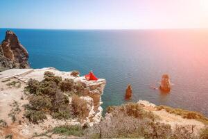 donna mare rosso vestire. bionda con lungo capelli su un' soleggiato riva del mare nel un' rosso fluente vestire, indietro Visualizza, seta tessuto agitando nel il vento. contro il fondale di il blu cielo e montagne su il spiaggia. foto