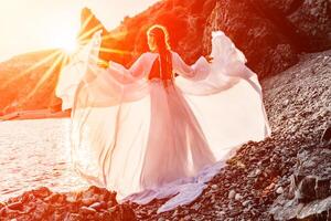 misterioso donna silhouette lungo capelli passeggiate su il spiaggia oceano acqua, mare ninfa vento ascolta per il onda. lanci su un' lungo bianca vestire, un' divine tramonto. artistico foto a partire dal il indietro senza un' viso